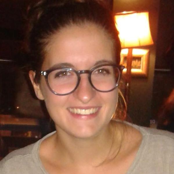 A headshot of Mirta Roncagalli smiling and wearing glasses with a lamp in the background